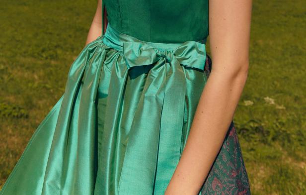 Nahaufnahme eines grünen Dirndls mit Schleife vor grünem Hintergrund.