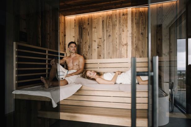 Ein Paar entspannt in einer Sauna mit Holzverkleidung.