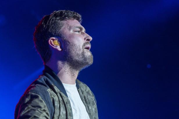 Ein Mann mit Bart und In-Ear-Kopfhörern singt vor blauem Hintergrund.