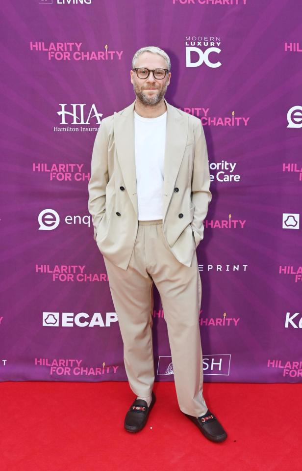 Seth Rogen posiert auf einem roten Teppich vor einem violetten Hintergrund.