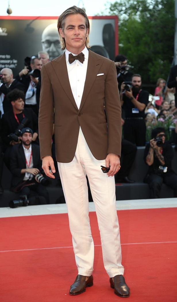 Chris Pine auf einem roten Teppich in einem braunen Anzug mit Fliege.