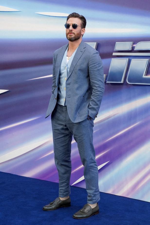 Chris Evans posiert in einem hellblauen Anzug und einer Sonnenbrille auf einem blauen Teppich.