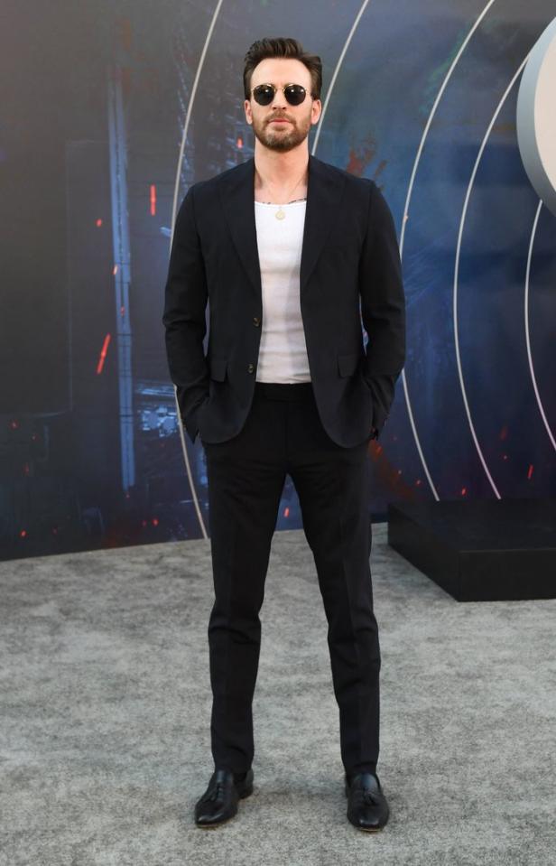 Chris Evans trägt einen dunklen Anzug und eine Sonnenbrille vor einem grafischen Hintergrund.