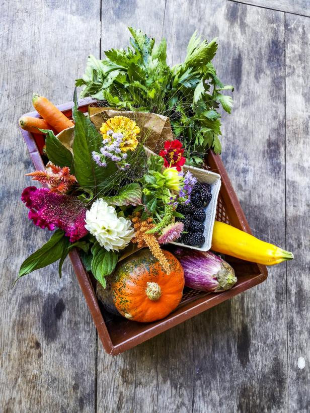 Ein Korb gefüllt mit Gemüse, Beeren und Blumen auf einem Holztisch.