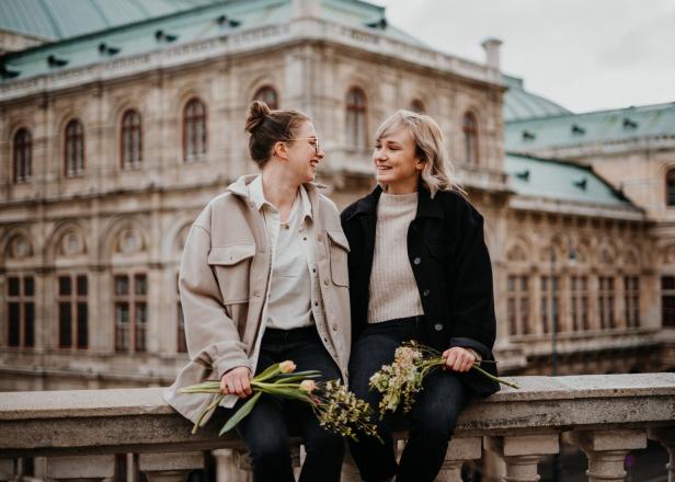 Zwei Frauen sitzen mit Blumen vor einem Gebäude in Wien und schauen sich an.