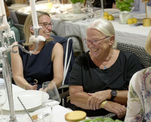 Zwei Frauen sitzen lachend an einem gedeckten Tisch.