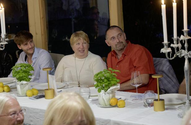Gäste sitzen an einem festlich gedeckten Tisch mit Kerzen und Basilikum-Gestecken.