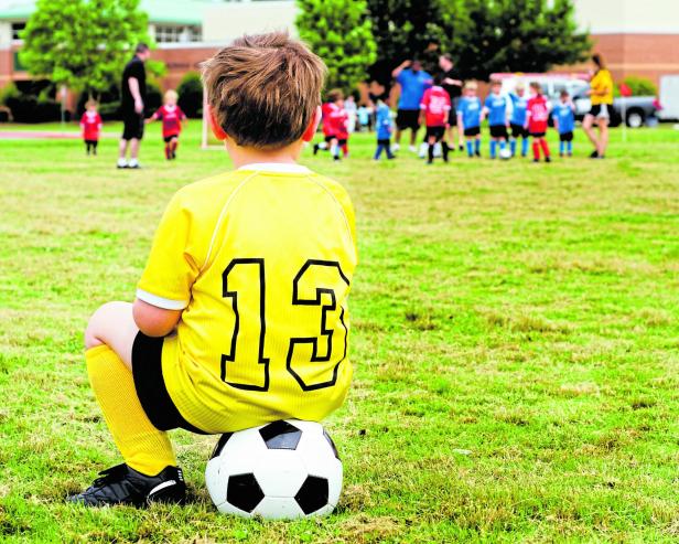 Young boy child in uniform watching organized youth soccer or football game from sidelines