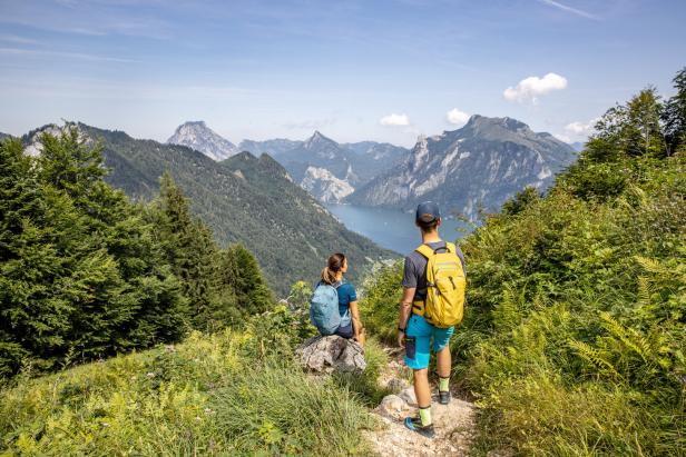 Zwei Wanderer genießen die Aussicht auf einen Bergsee und die umliegende Landschaft.