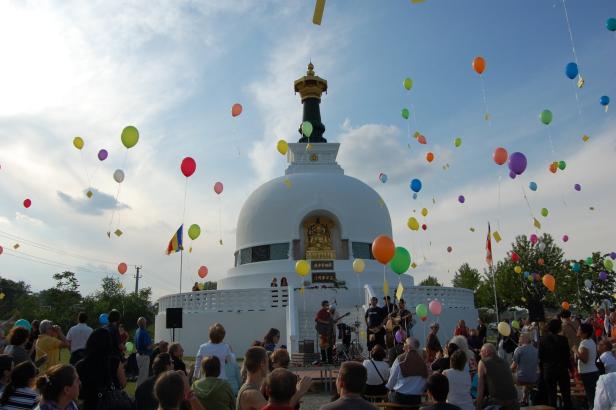 Eine buddhistische Stupa mit einer Menschenmenge und vielen bunten Ballons im Himmel.