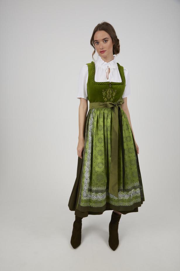 Eine Frau in einem grünen Dirndl mit weißen Bluse und braunen Stiefeln.