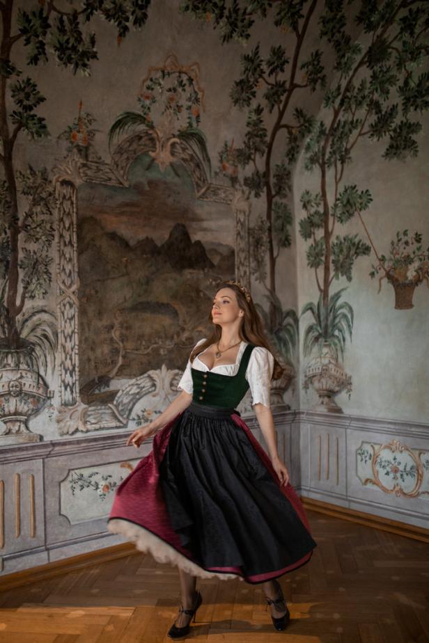 Eine Frau im Dirndl tanzt vor einem Wandgemälde in einem Schloss.