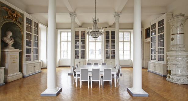 Ein großer Raum mit Bücherregalen, einem Tisch mit Stühlen und einem Kronleuchter.