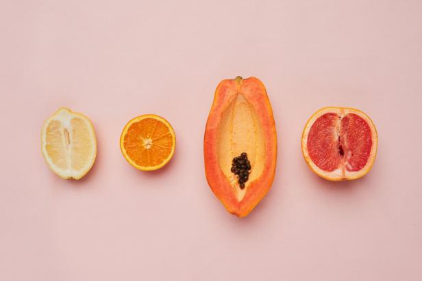 Eine halbe Zitrone, Orange, Papaya und Grapefruit liegen auf einem rosa Hintergrund.