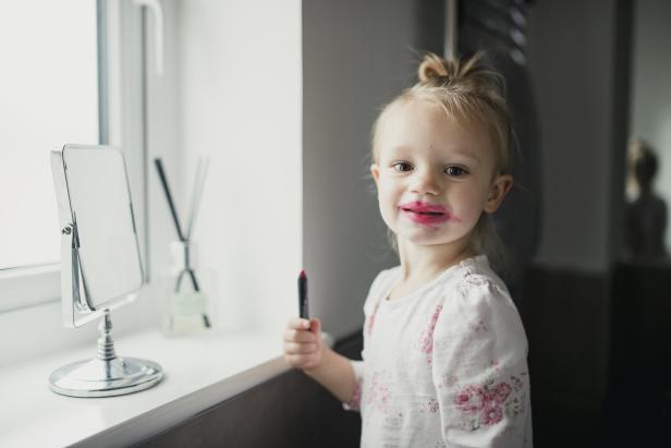 Ein kleines Mädchen hat sich mit Lippenstift beschmiert und hält einen Stift in der Hand.