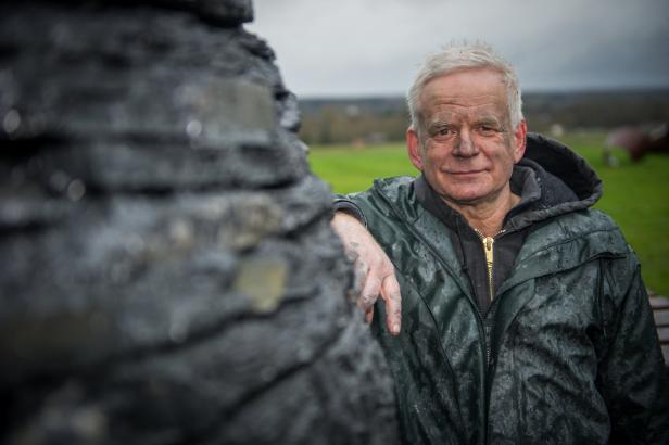 Ein Mann mit schmutzigem Gesicht lehnt an einer dunklen Skulptur.