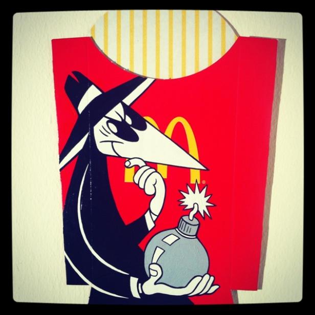 Ein Spy vs. Spy-Cartoon vor einer McDonald's-Pommes-Verpackung hält eine Bombe.