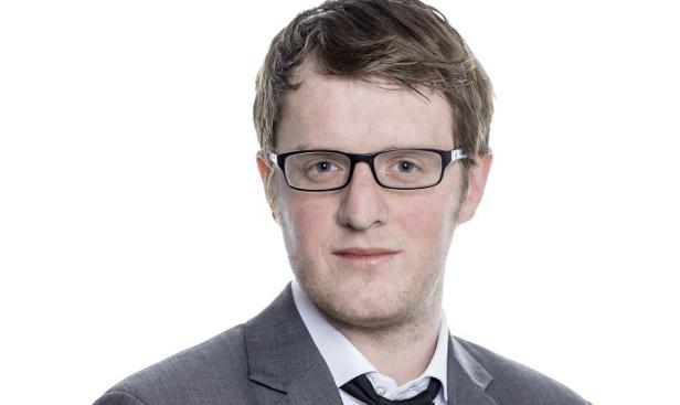 Ein Mann mit Brille, Anzug und Fliege vor einem weißen Hintergrund.