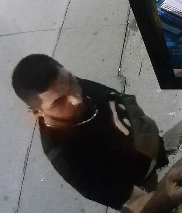 Ein Mann mit dunklen Haaren und einem schwarzen T-Shirt steht auf dem Bürgersteig.