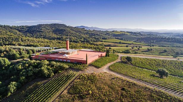 Luftaufnahme eines Weinguts mit einem ziegelroten Gebäude inmitten von Weinbergen und Hügeln.