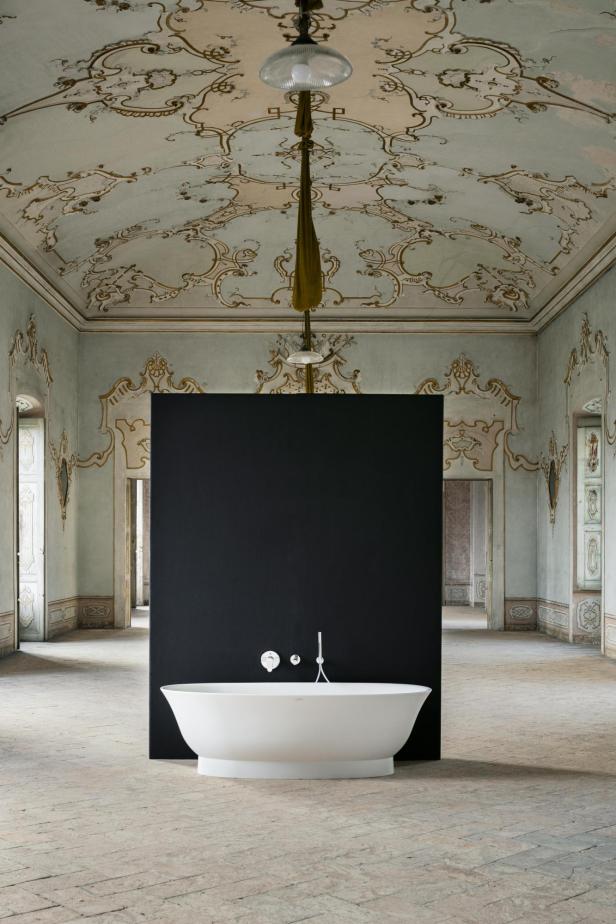 Eine freistehende Badewanne vor einer schwarzen Wand in einem verzierten Raum.