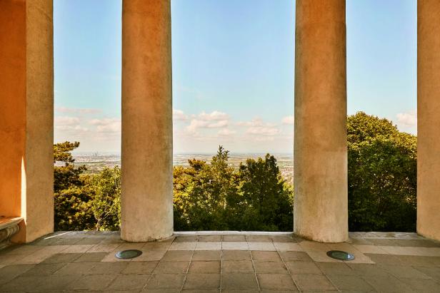 Blick durch Säulen auf eine grüne Landschaft und eine Stadt am Horizont.