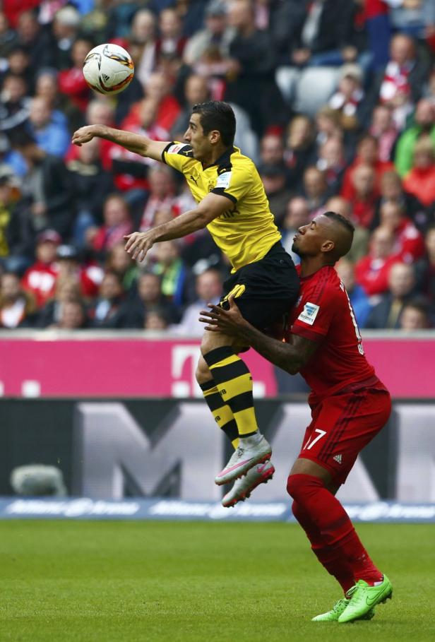 Ein Fußballspieler von Bayern München hebt einen Spieler von Borussia Dortmund in die Luft, der einen Ball wirft.