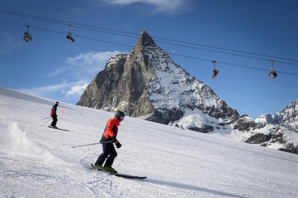 Skifahrer auf einer Skipiste mit Blick auf einen schneebedeckten Berg und Sessellifte.
