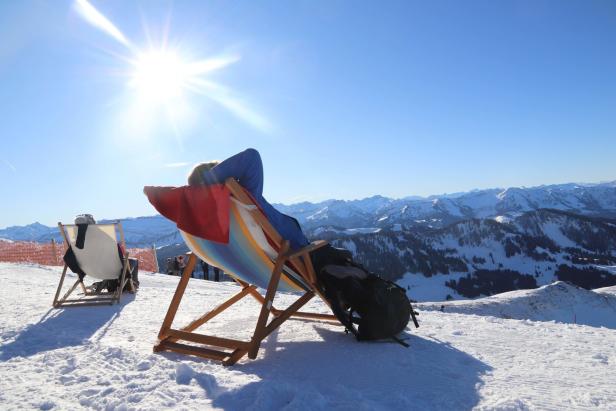 Eine Person entspannt in einem Liegestuhl im Schnee mit Blick auf die Berge.