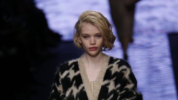 Eine Frau mit blonden, gewellten Haaren und einem schwarz-weißen Cardigan.