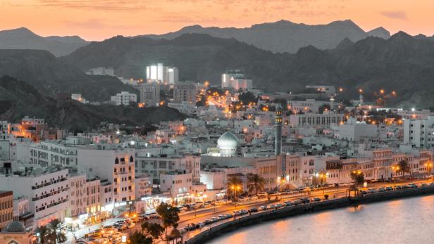 Blick auf Maskat, Oman, mit weiß getünchten Gebäuden und Bergen im Hintergrund bei Sonnenuntergang.