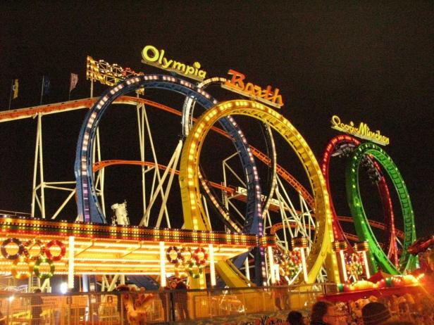 Die beleuchteten Achterbahnen „Olympia Looping“ und „Looping München“ auf einem Jahrmarkt bei Nacht.