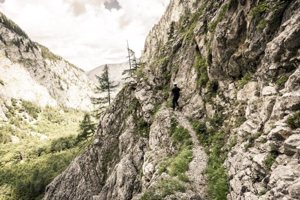 Ein Wanderer auf einem schmalen Pfad an einem steilen Berghang.