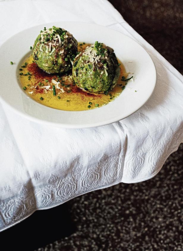 Zwei Spinatknödel liegen auf einem Teller mit zerlassener Butter und Parmesan.