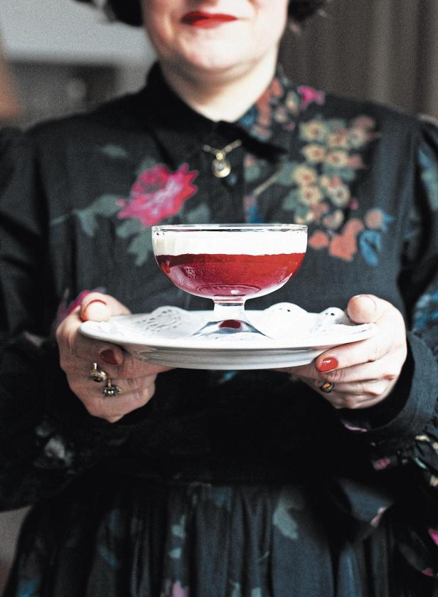 Eine Frau hält ein Dessert mit roter Flüssigkeit und einer weißen Schicht in einem Glas.