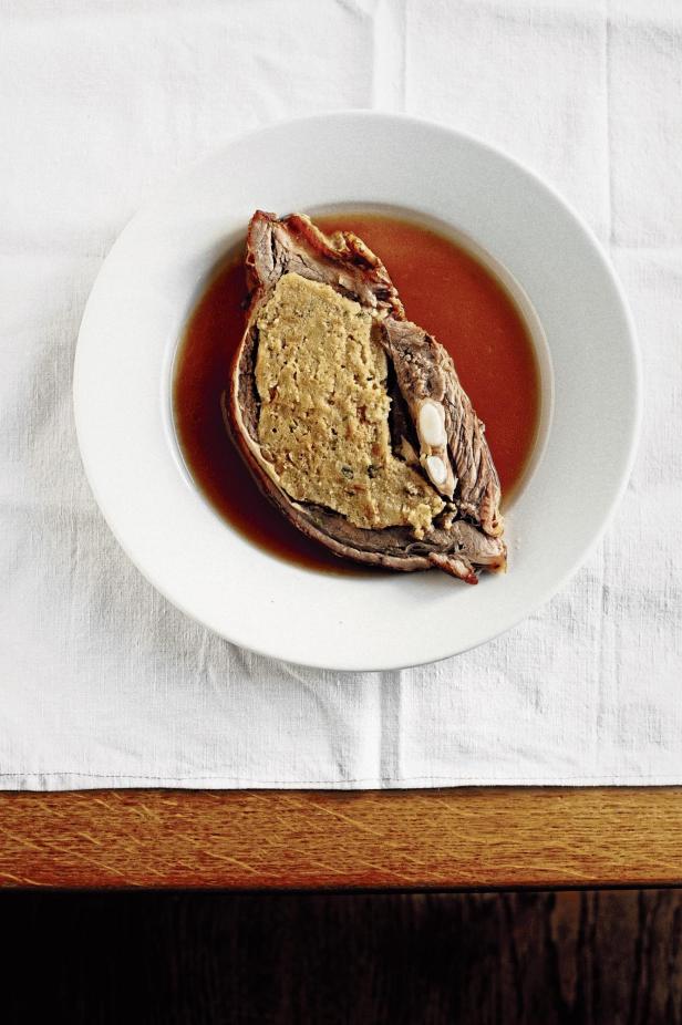 Ein Teller mit gefülltem Braten in Soße auf einer weißen Tischdecke.
