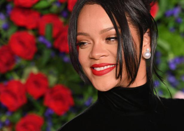 Die skurrilsten Ängste und Phobien der Stars Rihanna lächelt mit rotem Lippenstift und Perlenohrringen vor einem Blumenhintergrund.