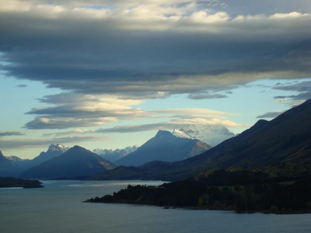 Eine ruhige Seenlandschaft mit Bergen im Hintergrund unter einem bewölkten Himmel.