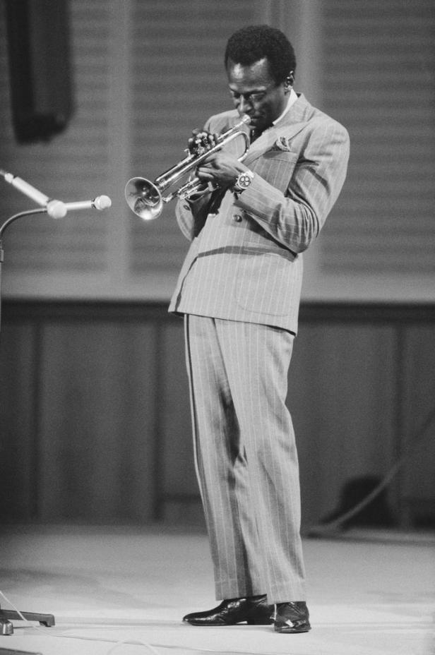 Miles Davis spielt Trompete in einem gestreiften Anzug auf einer Bühne.