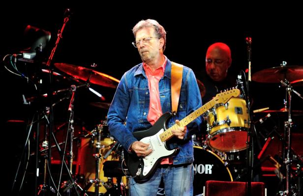 Eric Clapton spielt Gitarre auf einer Bühne vor einem Schlagzeug.