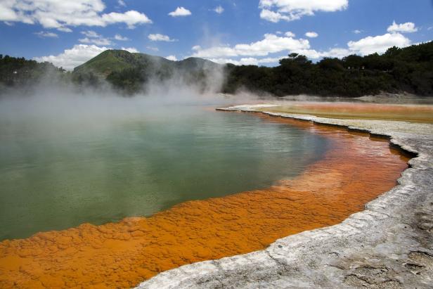 Der Wai-O-Tapu-See in Neuseeland mit seinem orangefarbenen Ufer und aufsteigendem Dampf.