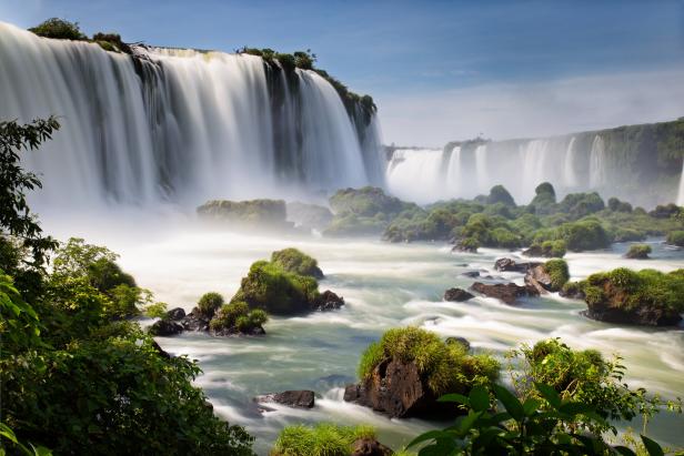 Die tosenden Iguazú-Wasserfälle stürzen in einen Fluss mit grünen Felsen.