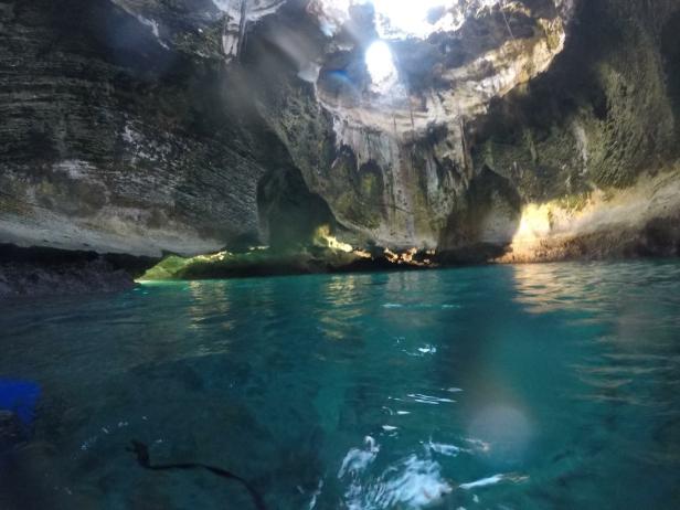 Sonnenlicht scheint in eine Höhle mit türkisfarbenem Wasser.