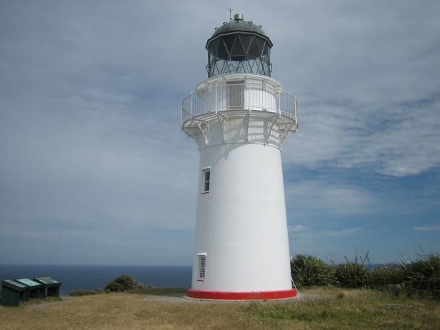 Ein weißer Leuchtturm steht an der Küste unter einem bewölkten Himmel.