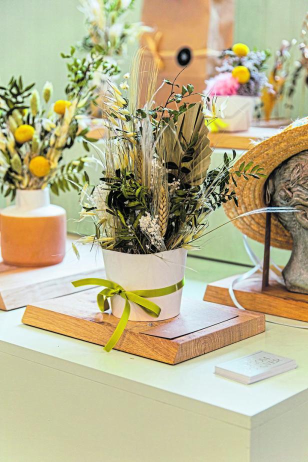 Ein Gesteck aus Trockenblumen und Gräsern in einem weißen Topf mit Schleife.