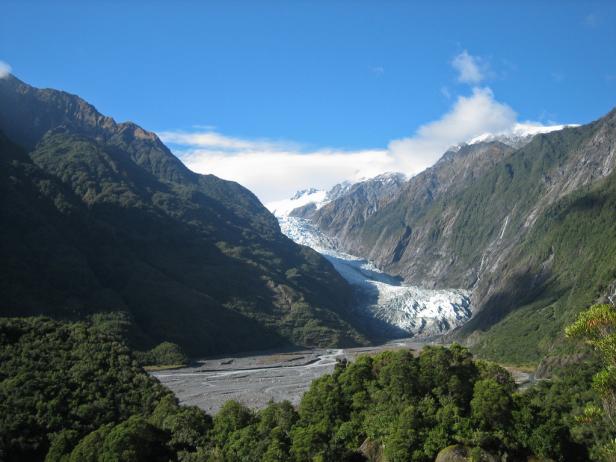 Der Franz-Josef-Gletscher zwischen bewaldeten Bergen unter blauem Himmel.
