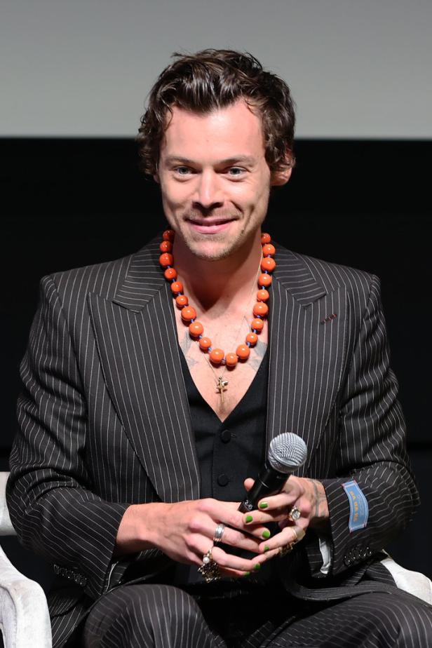 Harry Styles mit orangefarbener Halskette und grün lackierten Fingernägeln.