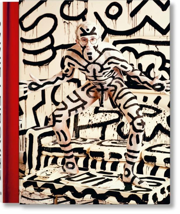 Ein Mann mit Brille, dessen Körper mit schwarzer Farbe im Stil von Keith Haring bemalt ist, posiert.