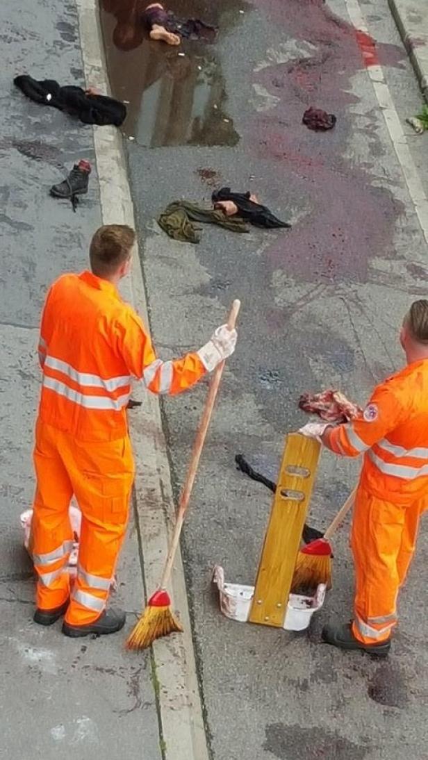 Zwei Arbeiter in orangefarbenen Overalls reinigen eine Straße mit Besen.