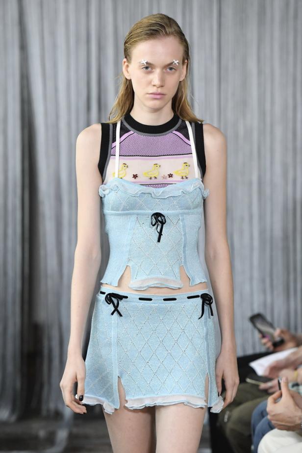 Ein Model präsentiert ein hellblaues, zweiteiliges Strickoutfit mit Schleifen und Entenmuster.